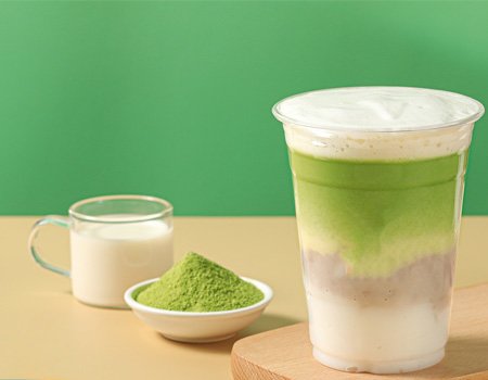 a cup of green milk tea, with a small bowl of matcha powder and milk next to it