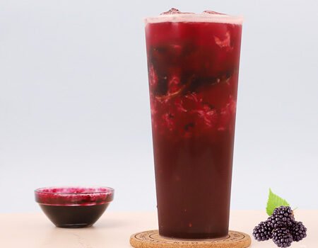 a cup of milk tea made from berry jam, with a small bowl of berry jam next to it