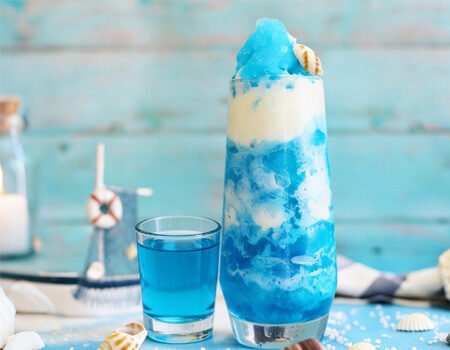 There is a cup of smoothie made of blue syrup and a small cup of blue syrup on the table