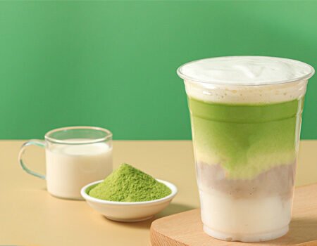 a cup of green milk tea, with a small bowl of matcha powder and milk next to it